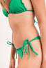 A woman models a vibrant green smocked bikini featuring a ruffled triangle top and adjustable side-tie bottoms.